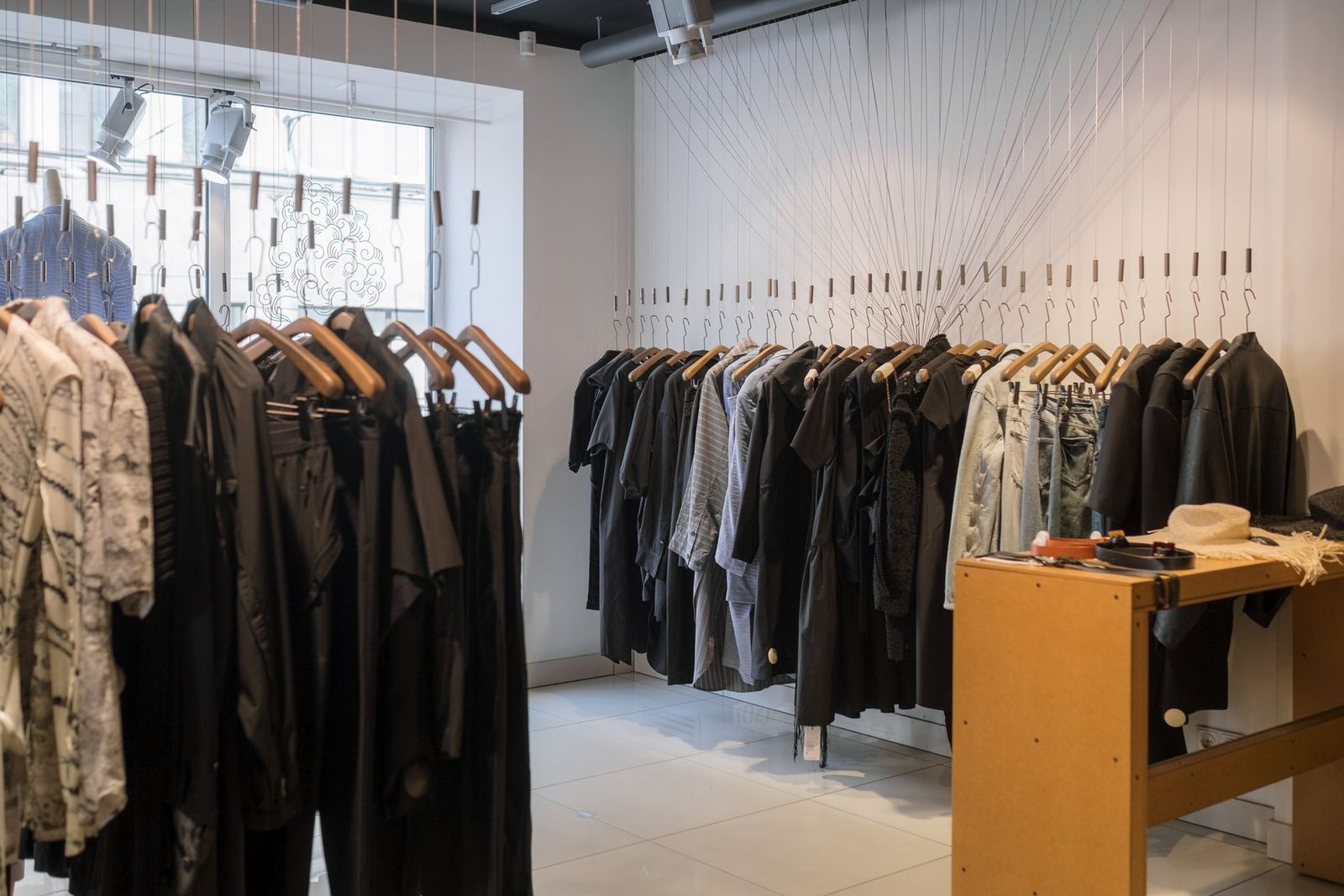 Clothing store with hangers suspended on fine cables from the ceiling and a timber counter