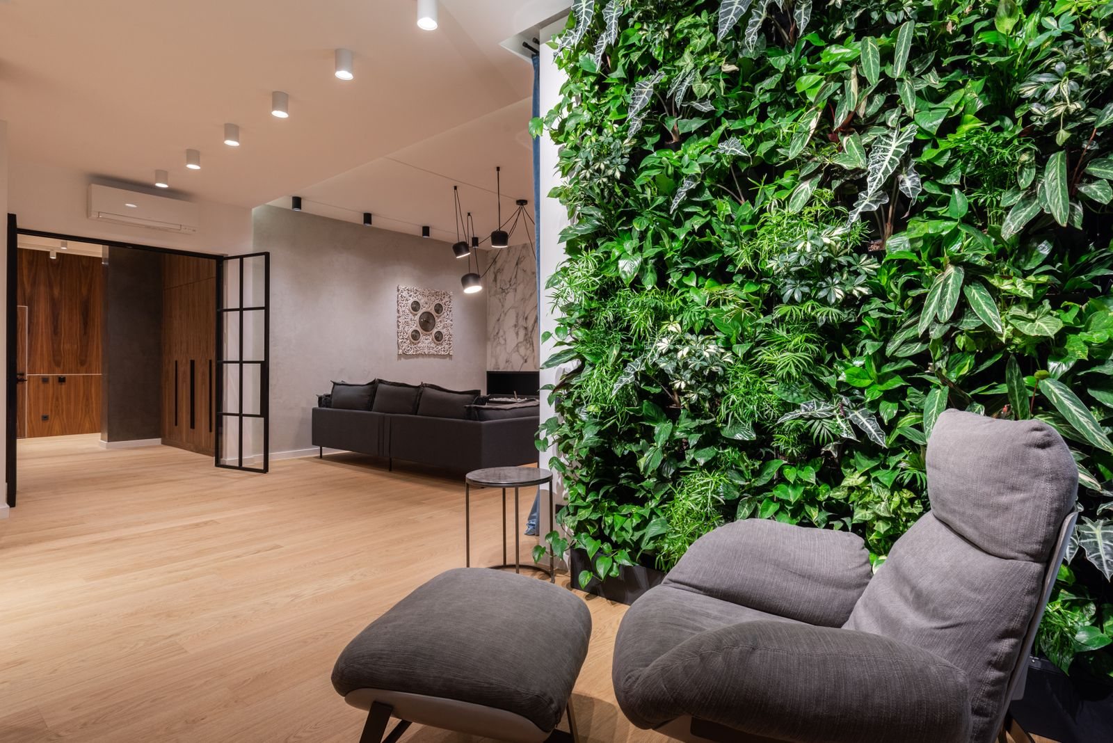 Living plant wall beside a grey lounge chair and footstool in an open-plan apartment