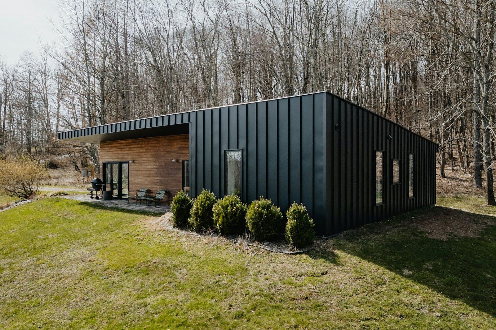 Single-storey house clad in black standing-seam metal with a timber-clad entrance recess