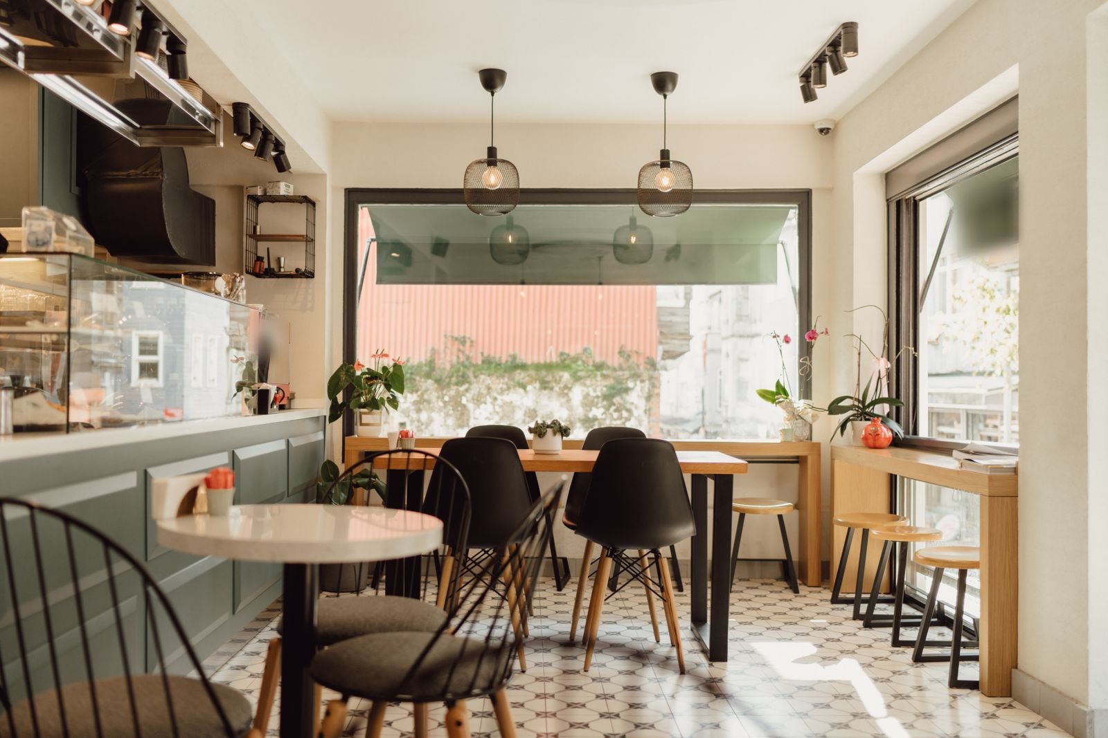 Small sunlit cafe with a counter and pastry case, two pendants, black chairs and a window bar with stools