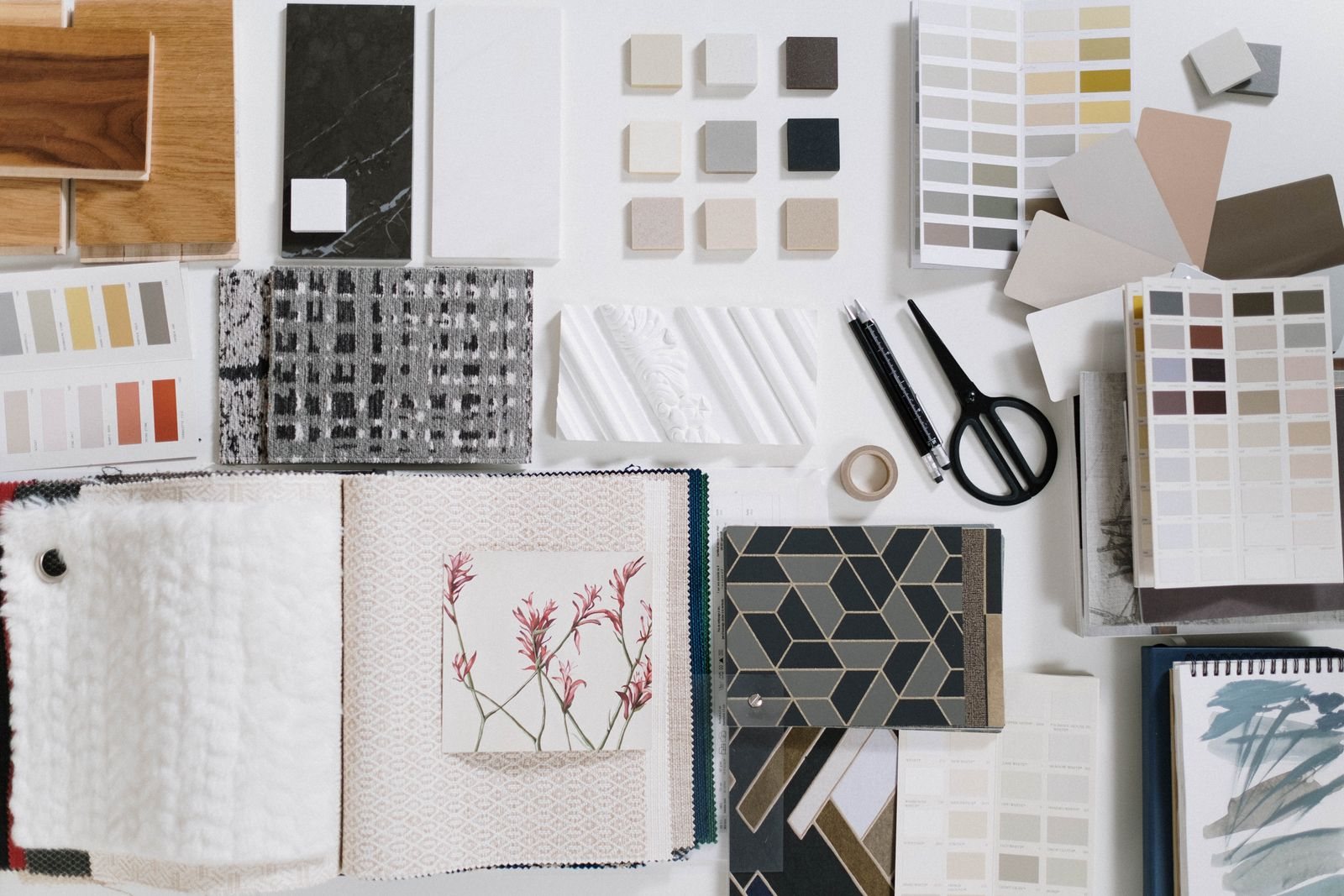 Flat lay of interior material samples: wood, stone, tile chips, fabric books and paint fans